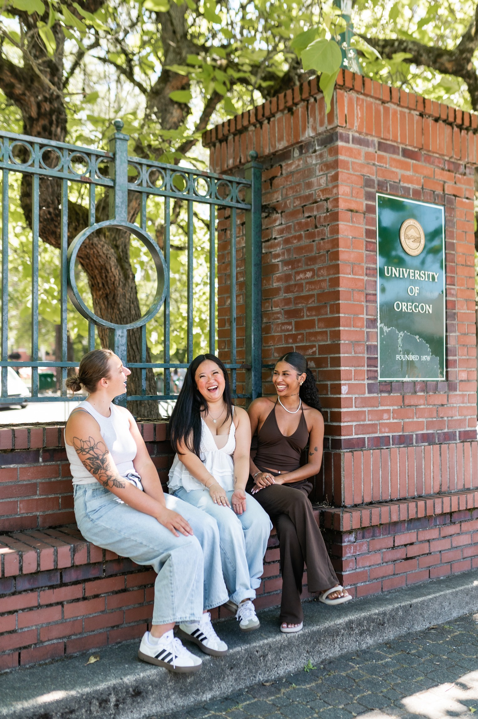 Three friends sitting on a bench at the entrance to the University of Oregon campus