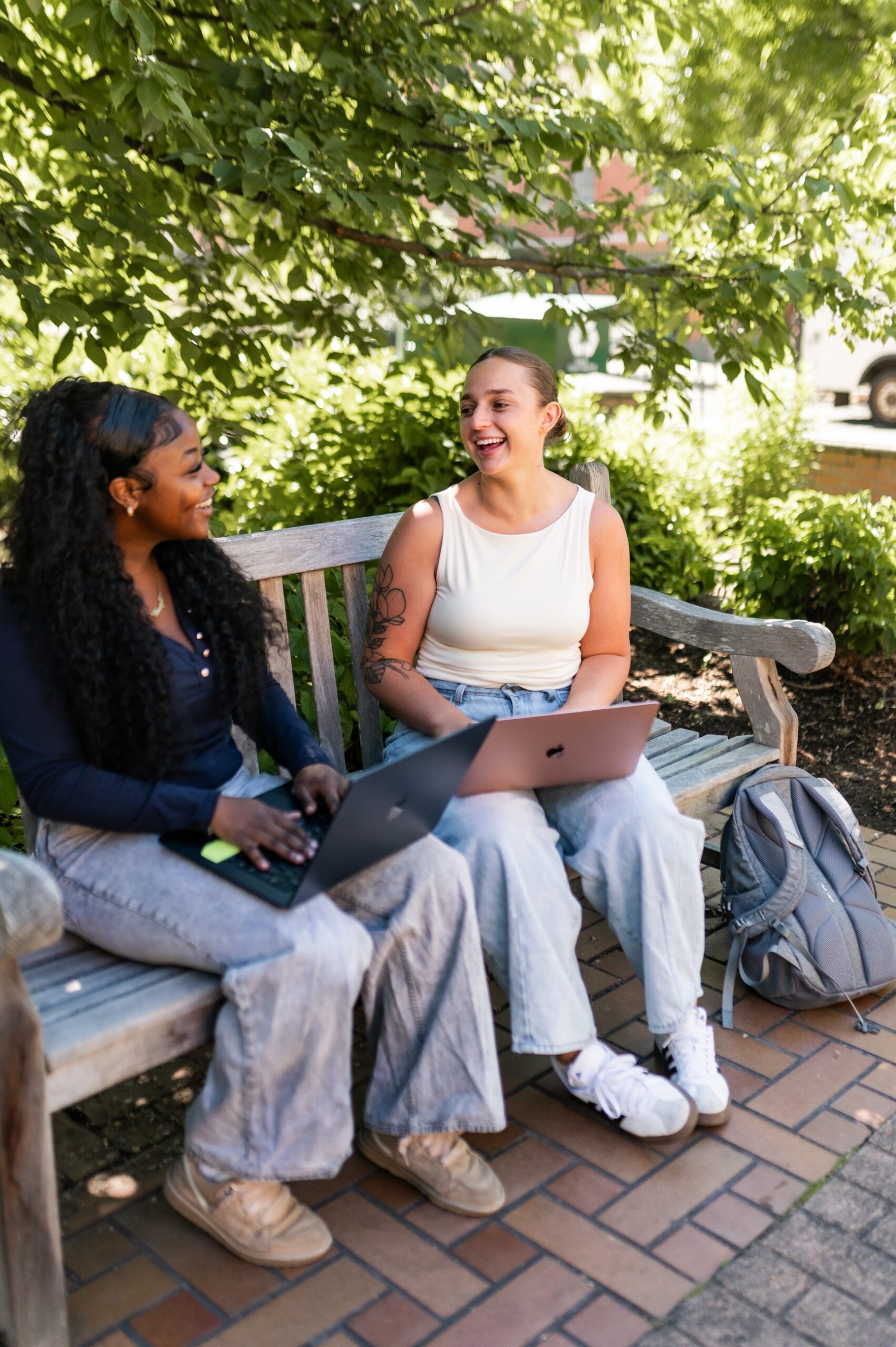 Two women working on their laptops on a bench on the UO campus