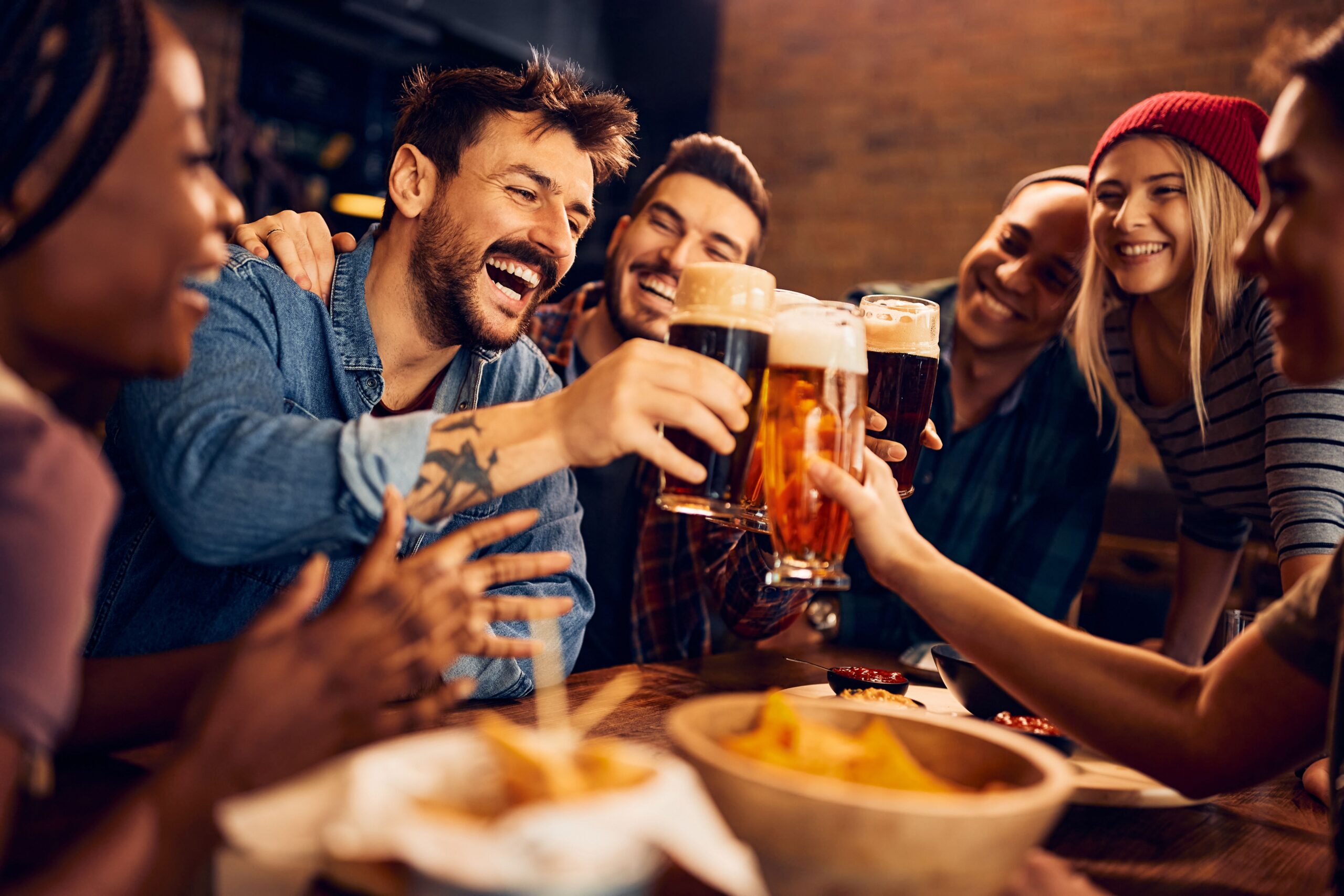 friends clinking beer glasses at bar scaled